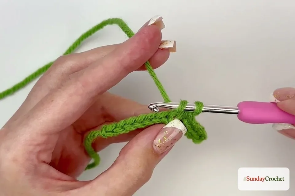Hands work crochet stitches into the foundation chain to shape one side of the leaf