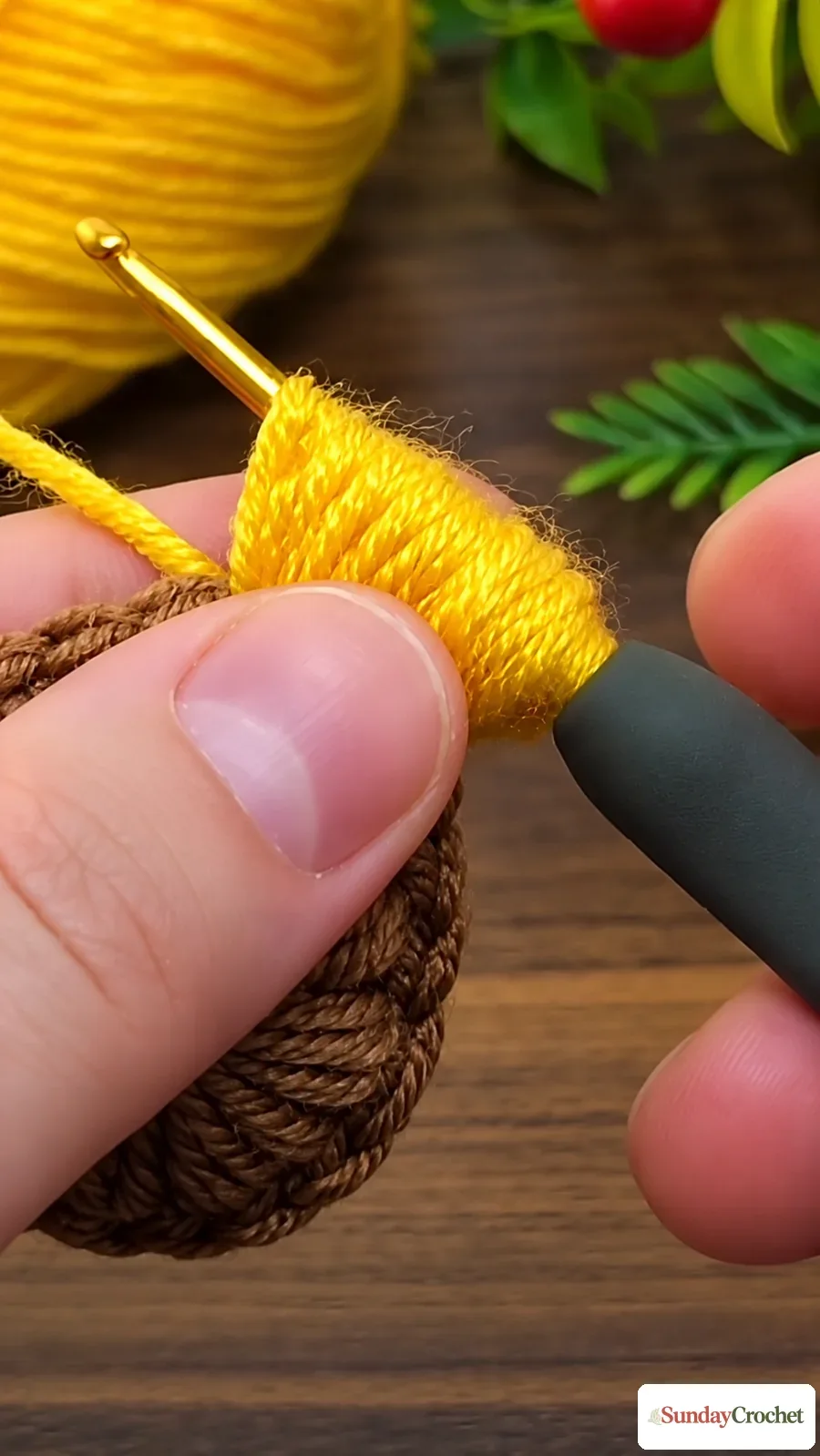Close-up of a yellow crochet petal being shaped beside the textured brown center