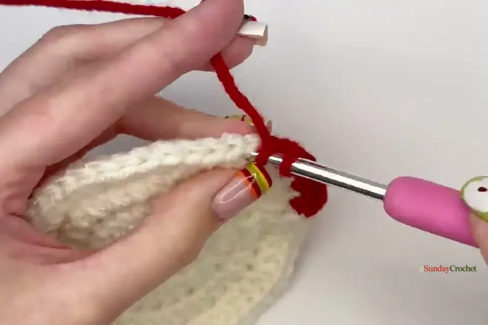 Hands crochet the red outer round that shapes the top indentation of the apple