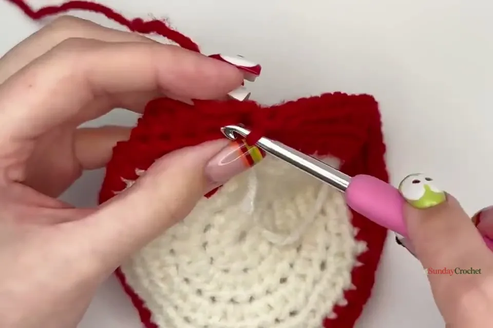 The red rim rises as hands crochet the final half double crochet round of the dish