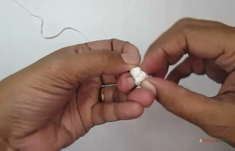 A tiny white crocheted shoe is turned right side out after its third round