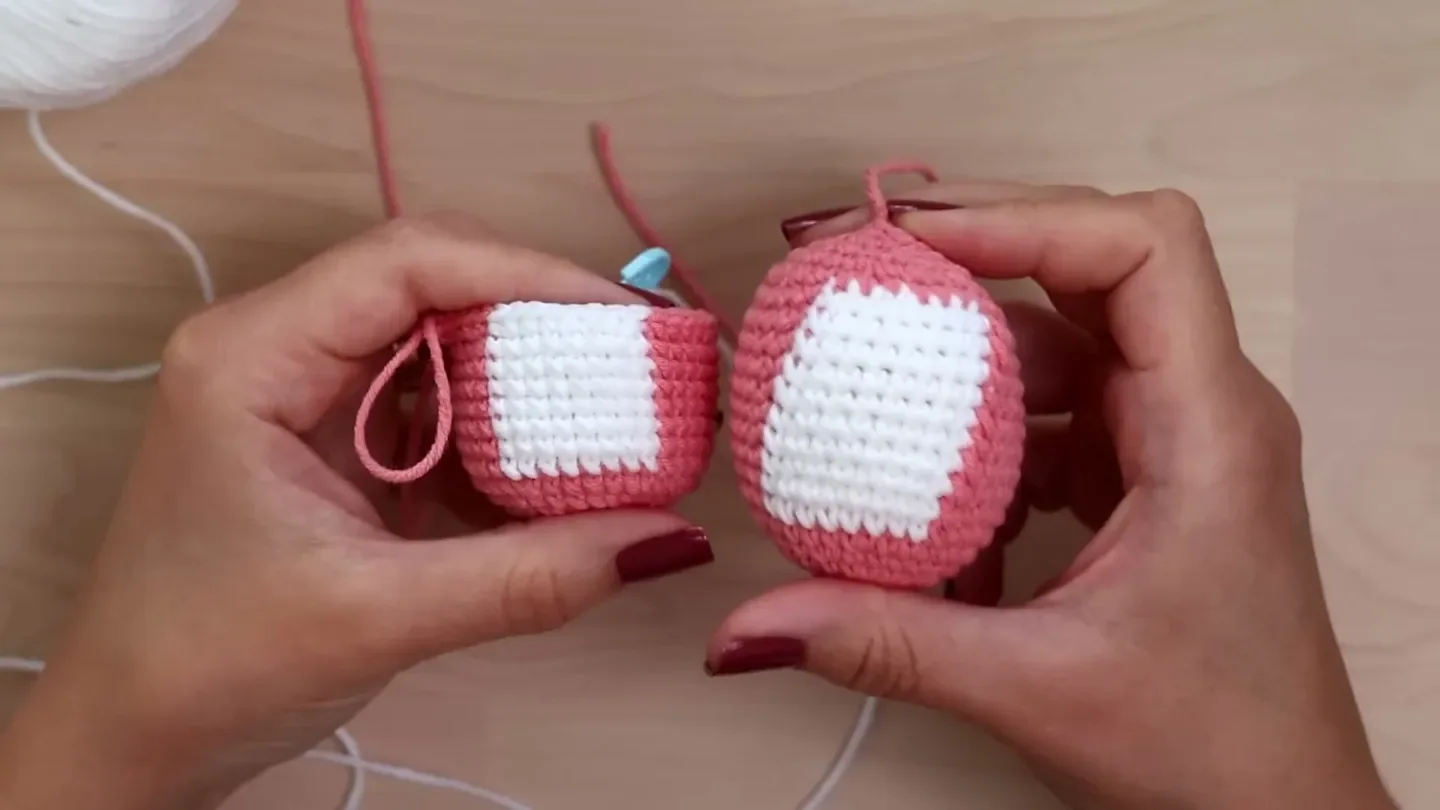 Two finished pink crochet samples with white panels are held side by side to compare stitch alignment.