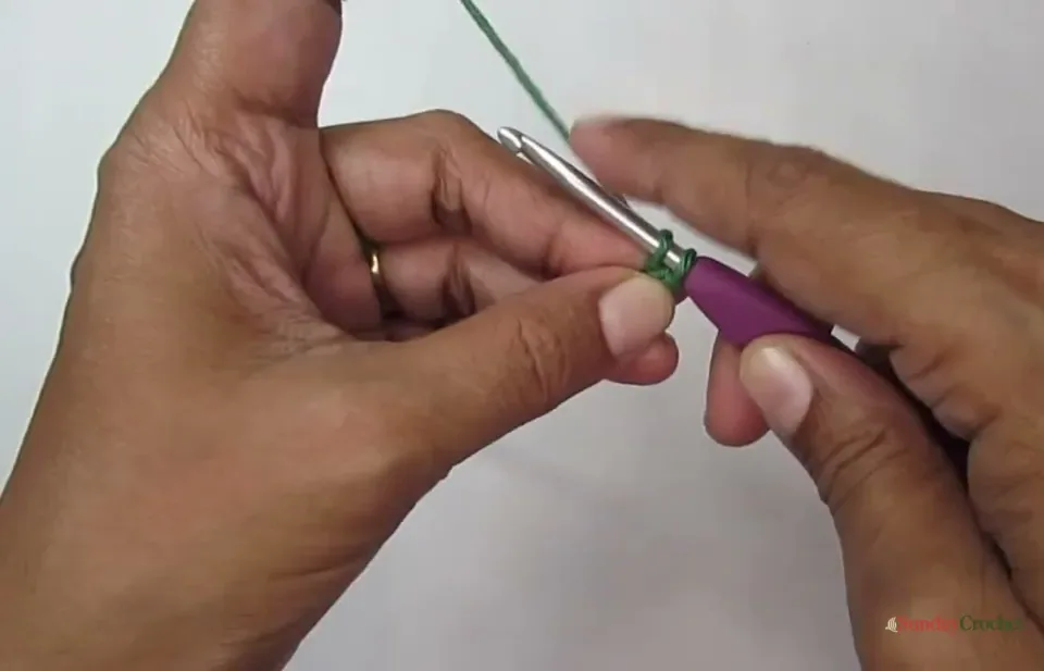 Hands crochet the small green cord that forms the pumpkin stem
