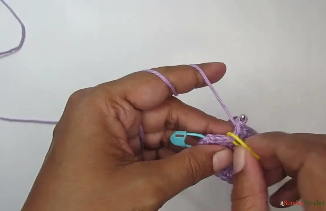 A growing lavender phone pouch held while single crochet rounds build up from its oval base