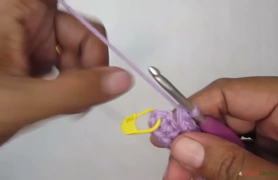 Hands crochet the curved end of the lavender pouch base beside a yellow stitch marker