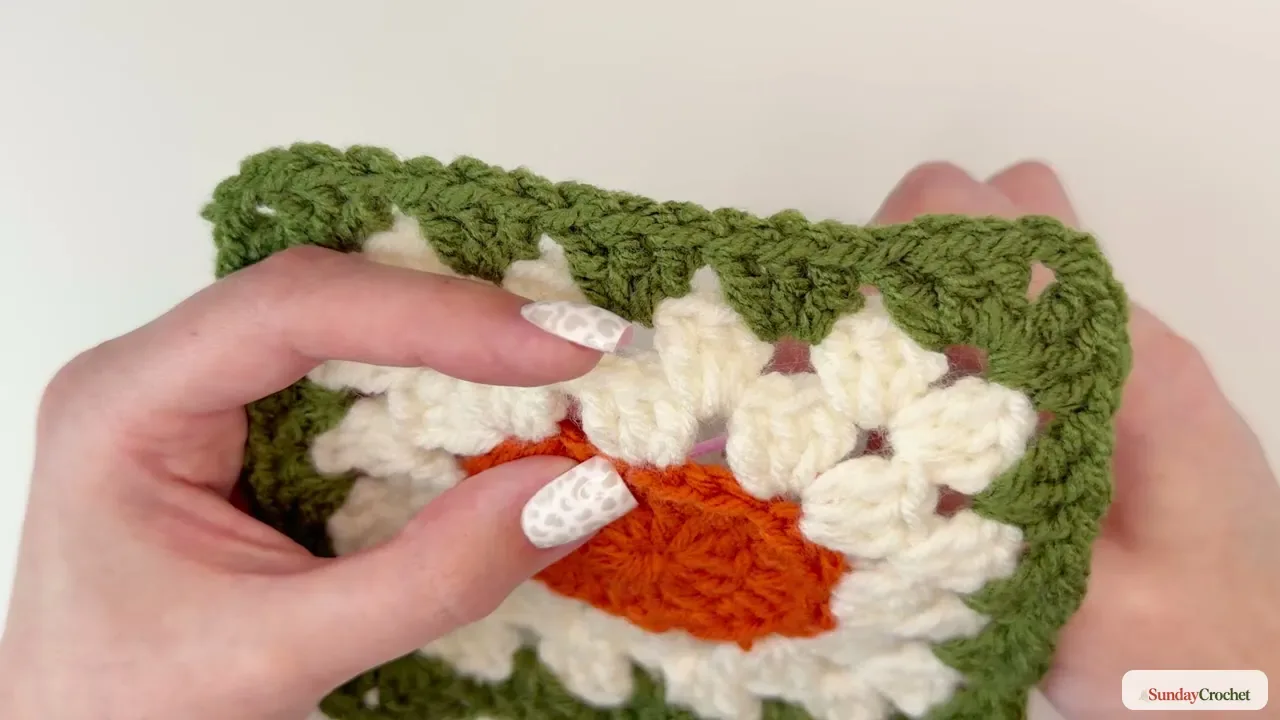 Tapestry needle places brown yarn at the top center of the orange pumpkin motif to form its stem