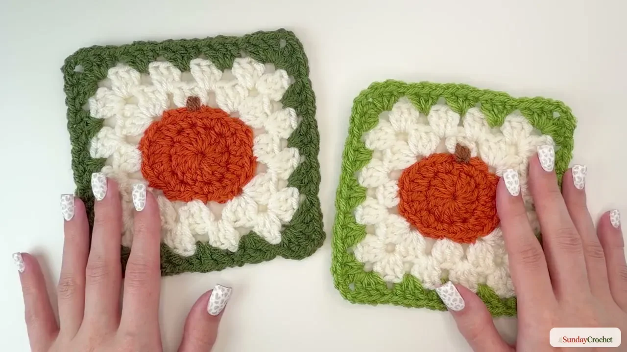 Finished pumpkin granny square with orange center, cream clusters, green border, and brown stem