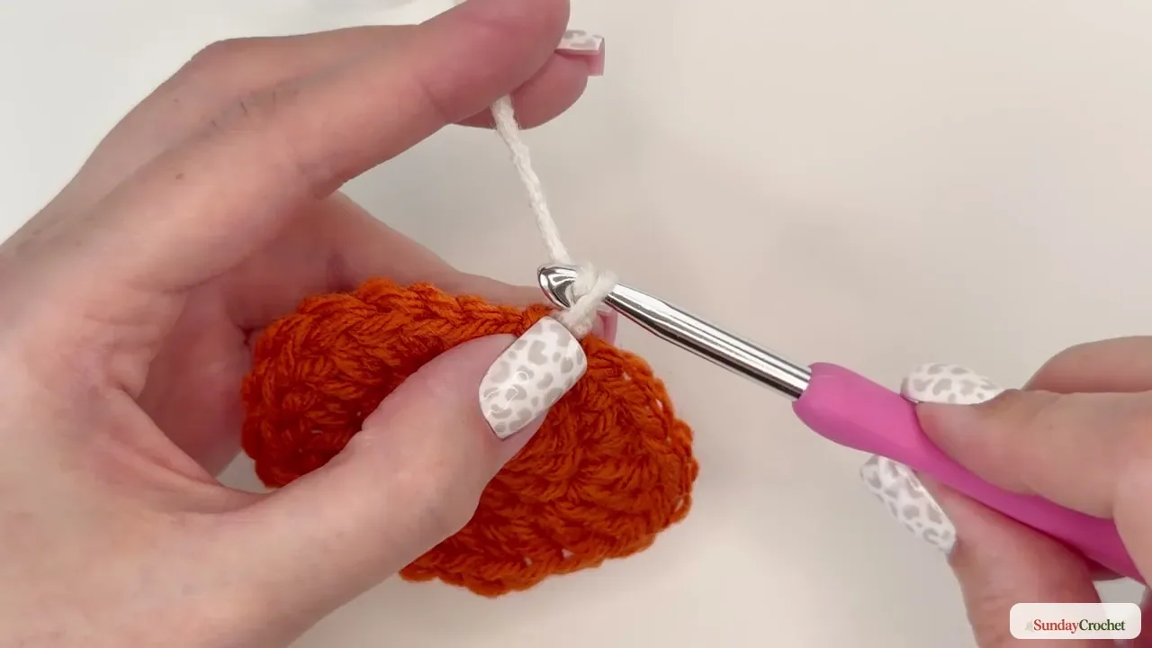Cream yarn being joined at the back loop of the orange pumpkin center