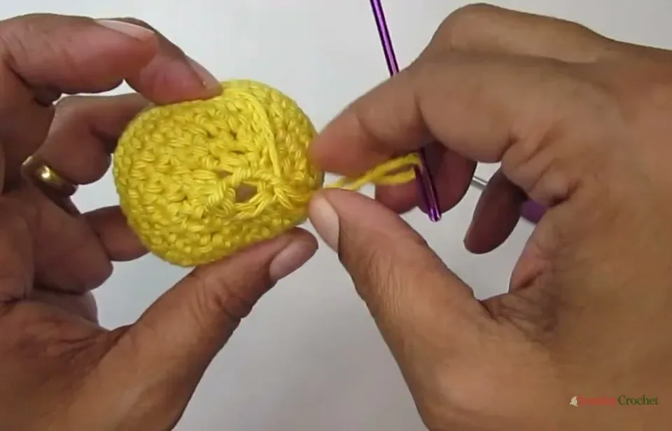A yarn needle draws three long shaping ribs through the stuffed pumpkin from top to bottom