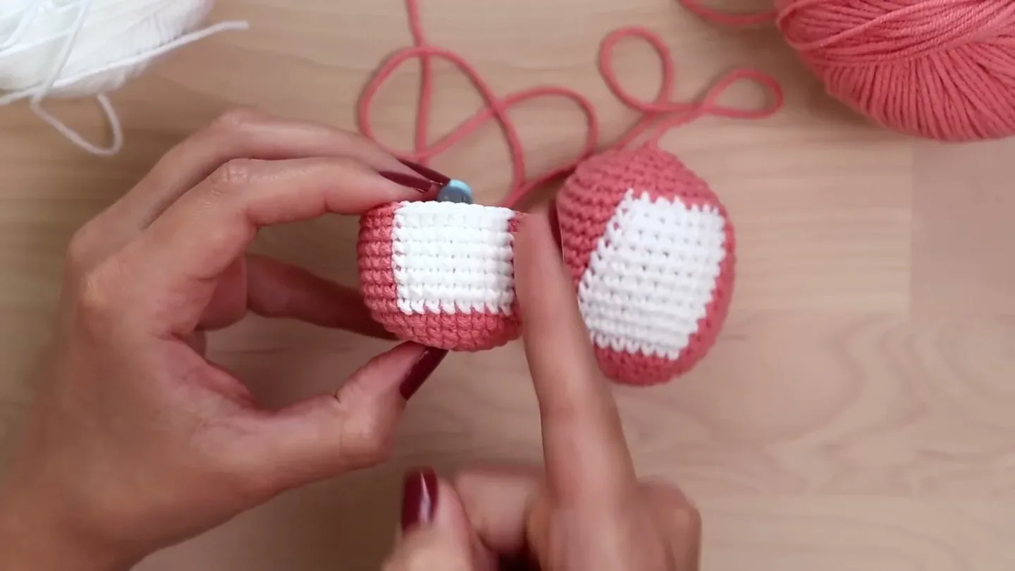 A hand compares two pink amigurumi samples with white panels, one flatter and more aligned than the other.