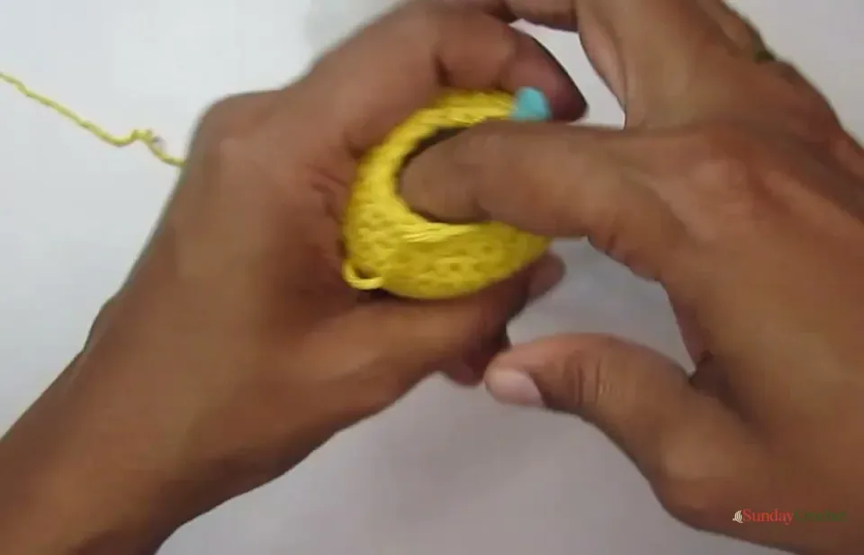 The open yellow pumpkin body is filled with fiber stuffing before the final decrease rounds are closed