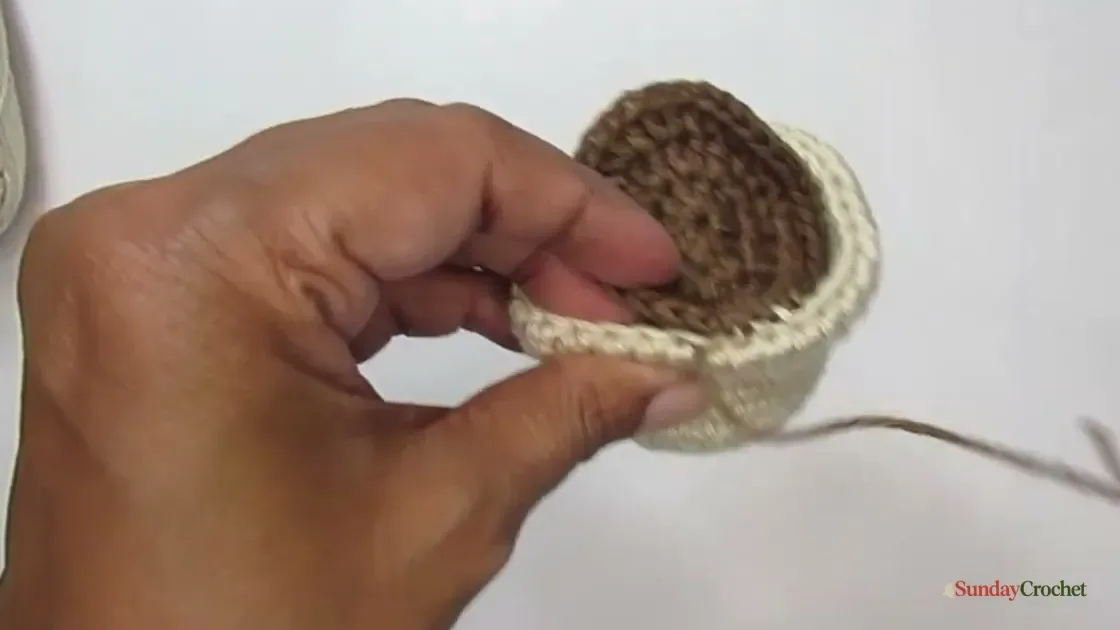 A brown crocheted soil circle is being sewn to the cream pot opening.