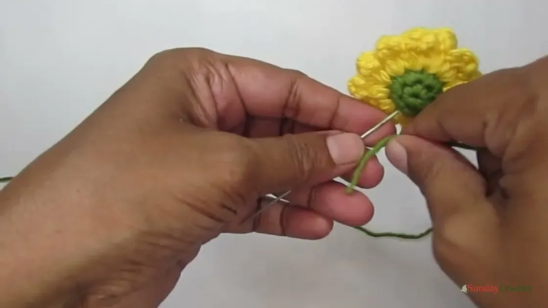 Green yarn is wrapped around the wire behind the flower as the stem is assembled.