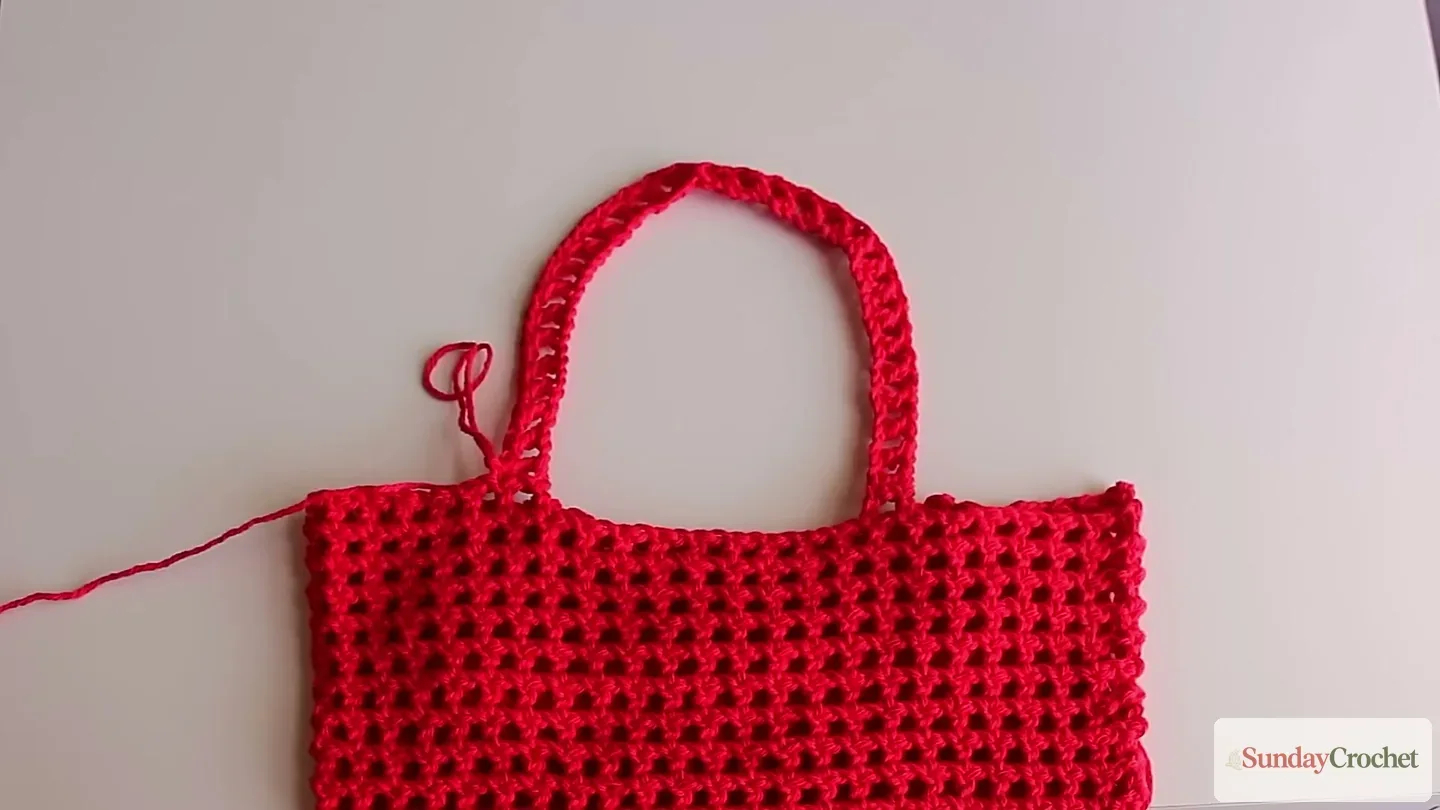 The finished red mesh tote has an open stitch pattern and a long crocheted shoulder strap
