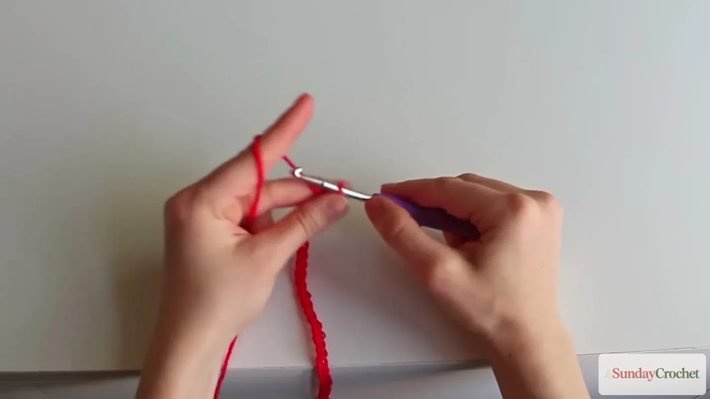 Hands begin the red crochet mesh bag by chaining its foundation with a purple hook