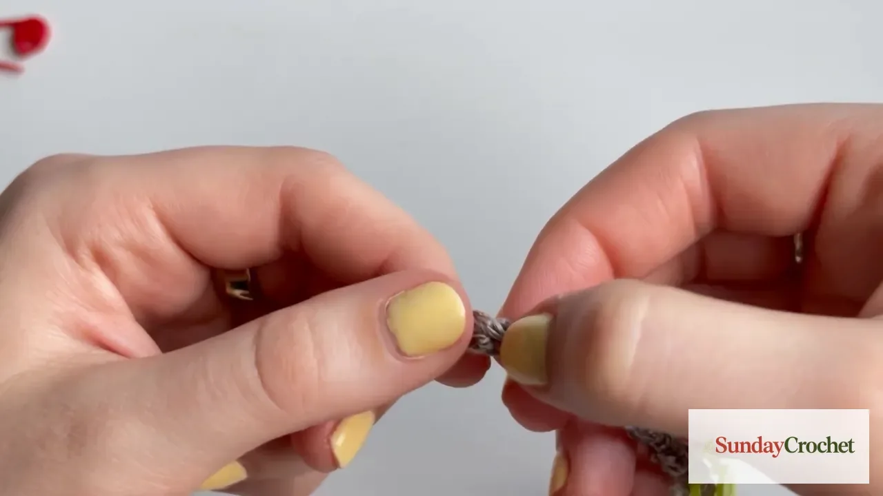 Hands hold the first taupe crochet chain for the poncho foundation