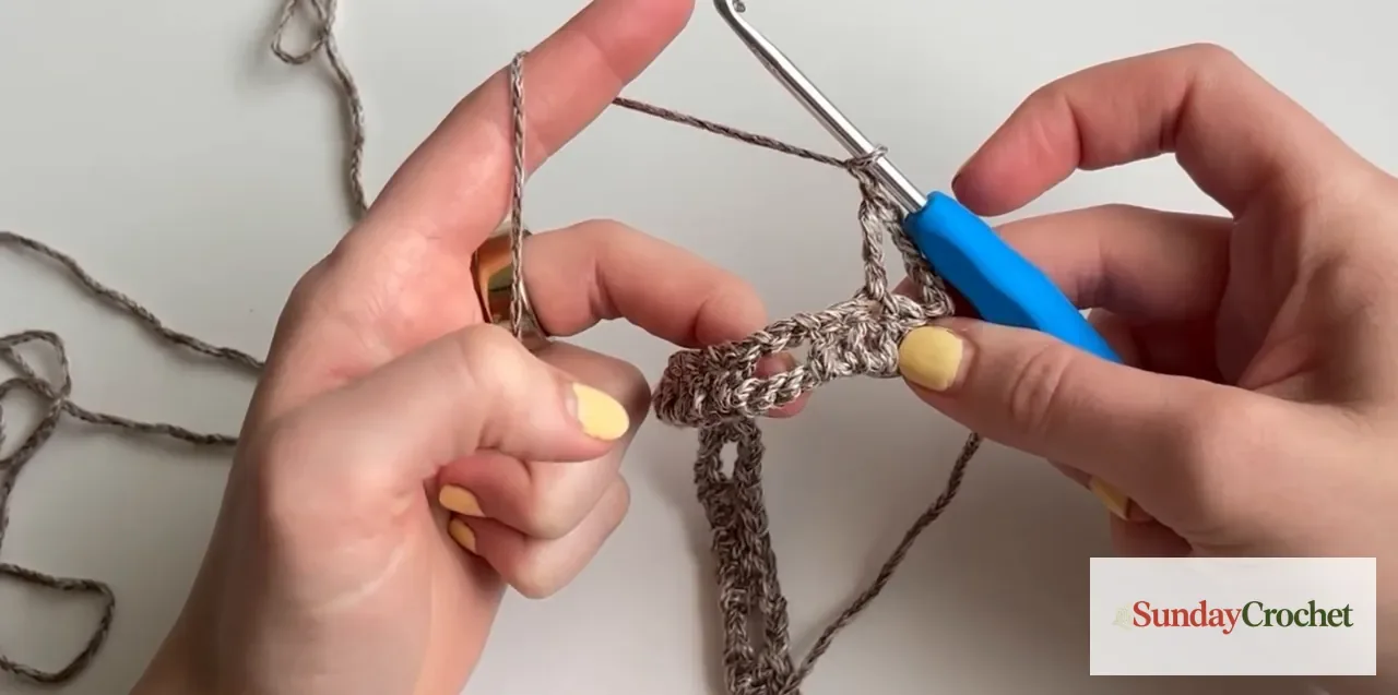 Hands work treble crochets with chain-one spaces across a mesh row