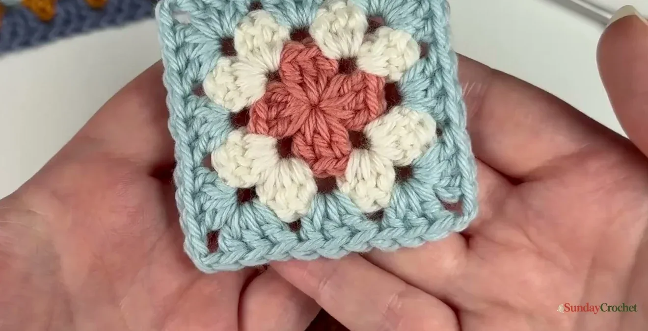 A blocked flower-center granny square lies flat with clean right-angle corners