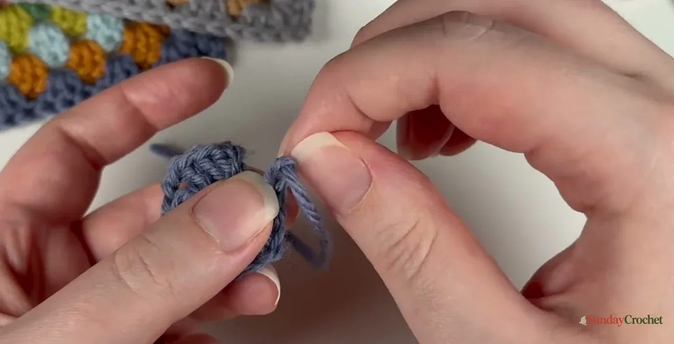 A crochet hook draws the yarn tail through the last stitch to make an invisible join