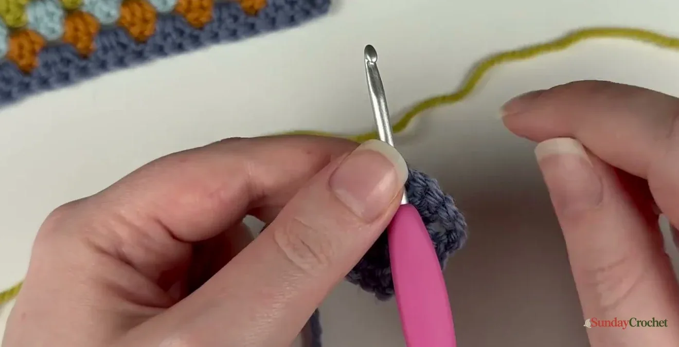 The next yarn color is joined through a corner space rather than along the side of the square