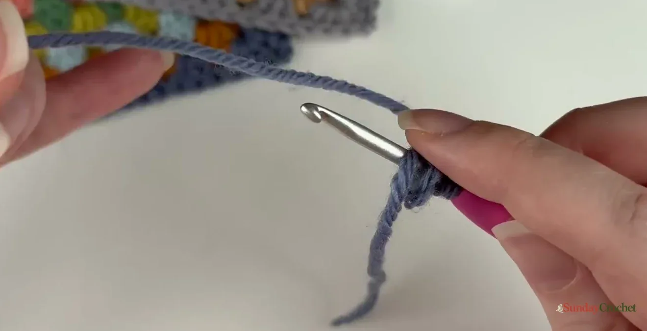 The starting yarn tail is held over the crochet hook so the first round can crochet over it