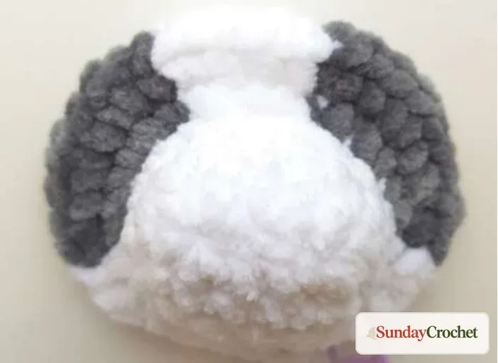 Close view of gray eye patches crocheted into the white plush panda head