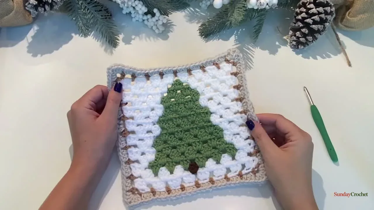 Finished granny-stitch Christmas tree square with a light background and tan border