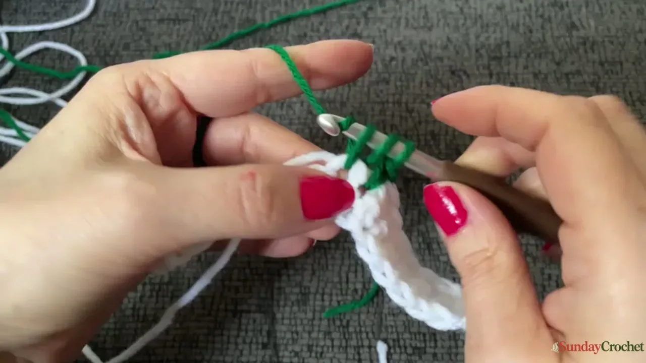 Hands crochet a green puff stitch into the cream background of a Christmas tree square