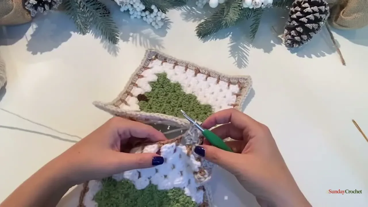 Hands join two Christmas tree granny squares along one edge with a slip stitch