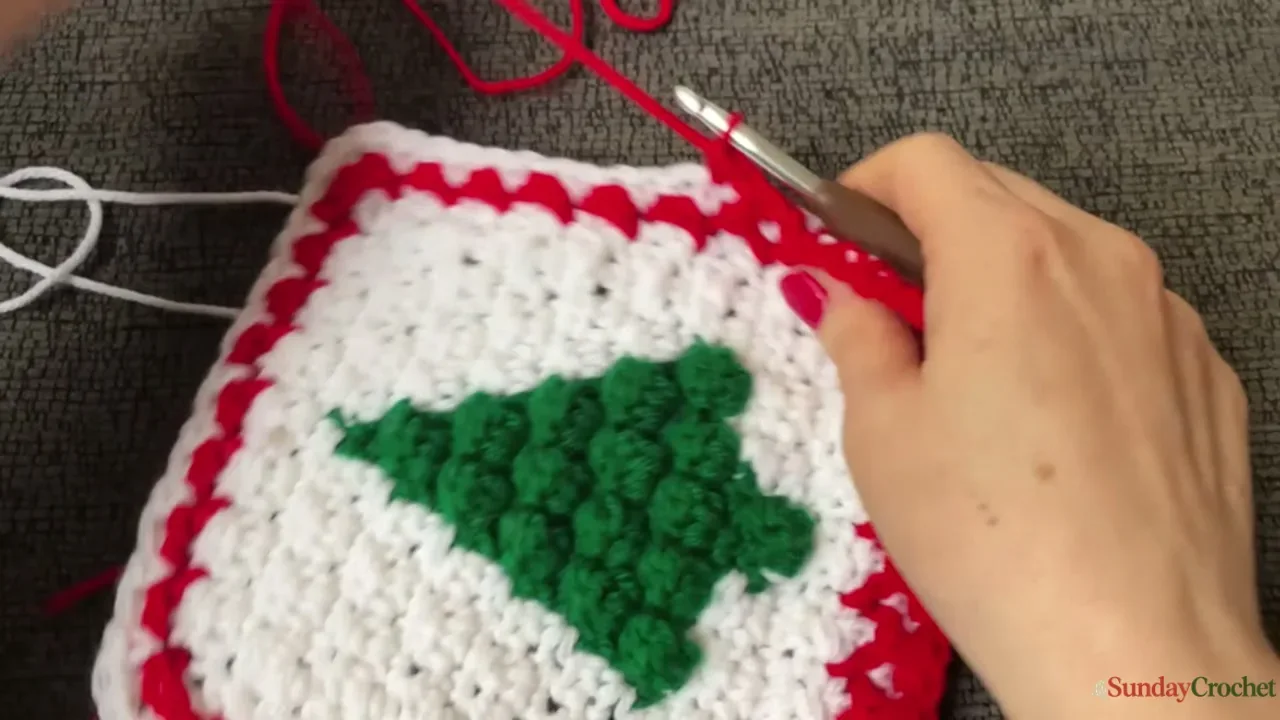 Hands join two red-edged Christmas tree squares with a raised single-crochet seam