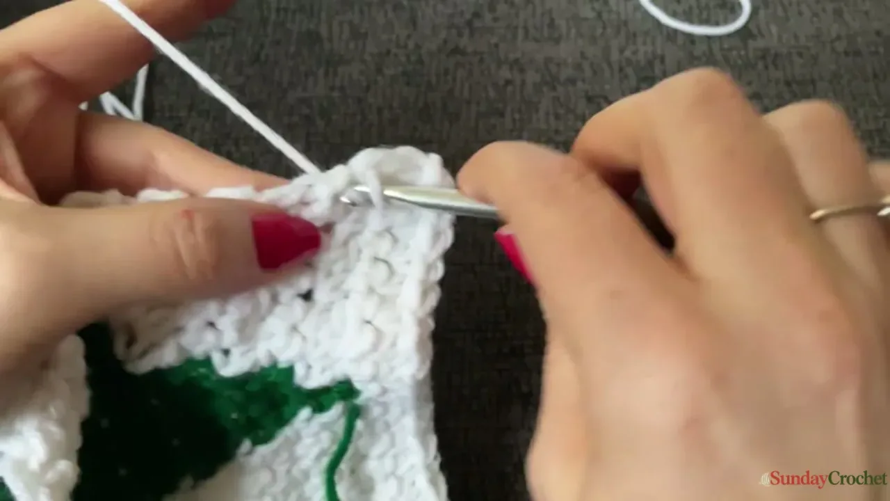 Red chain arches are crocheted around the outer edge of the cream Christmas tree square