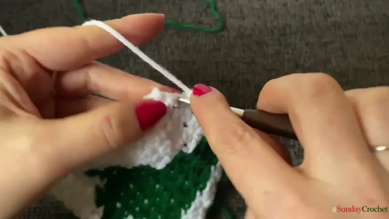 A cream corner of the Christmas tree square is edged with red crochet