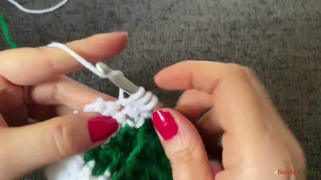 Hands work the narrowing green Christmas tree motif against cream crochet fabric